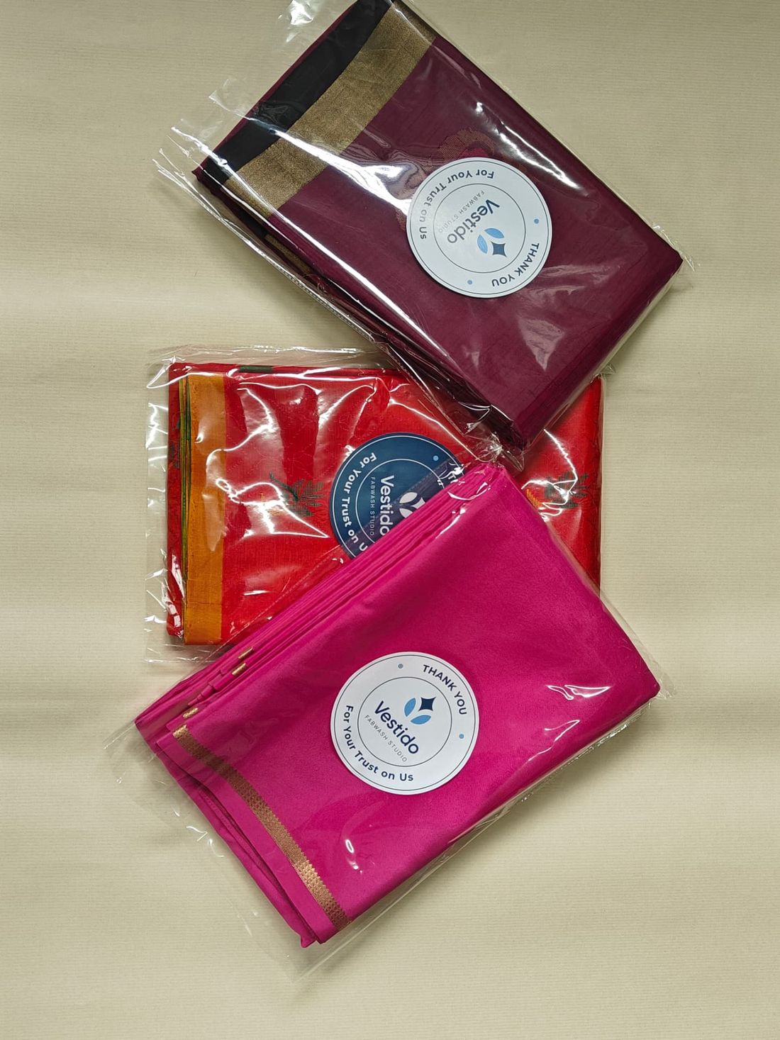 Maroon, orange and pink silk sarees roll polished, folded and packed for doorstep delivery